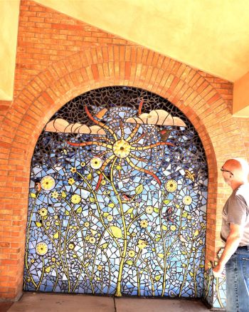 Author studies ceramic mosaic of sun, sky, clouds and flowers at Albuquerque Academy in New Mexico