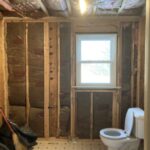 Small bathroom with walls and ceiling ripped out. Only toilet left standing.